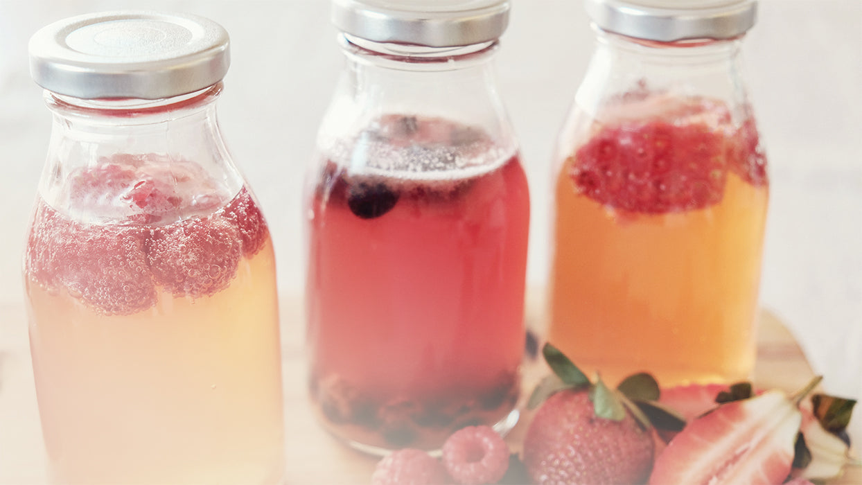 drei Glasflaschen Kombucha mit Fruechten Erdbeeren